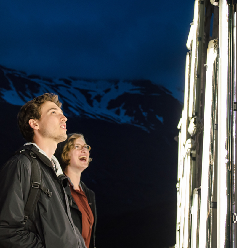 Two people look up at illuminated structure in the nighttime.