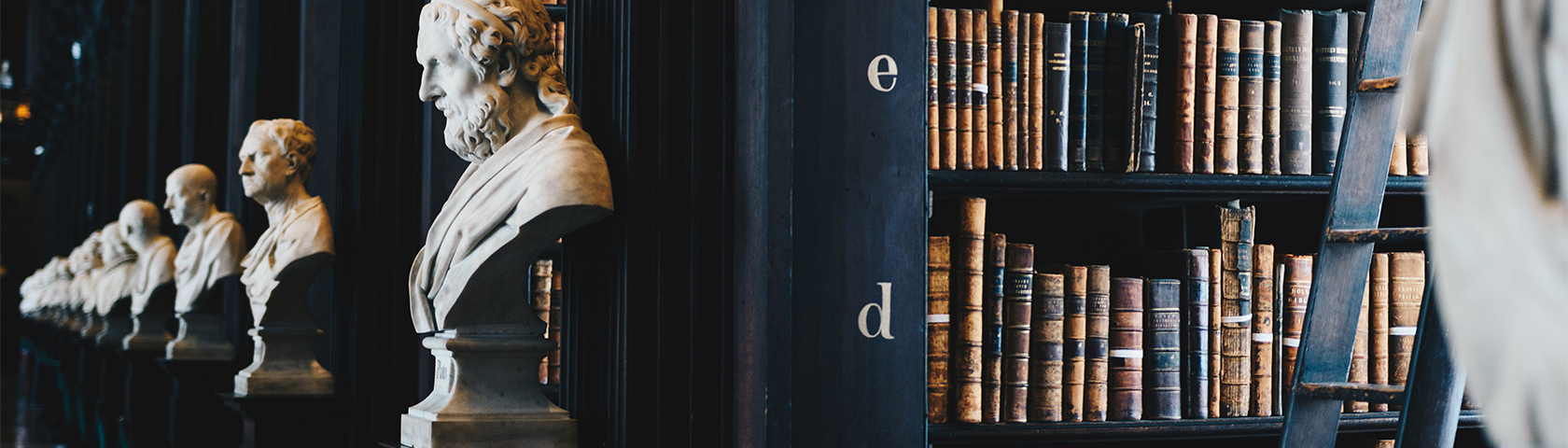 A lineup of busts of philosophers and books on a shelf.