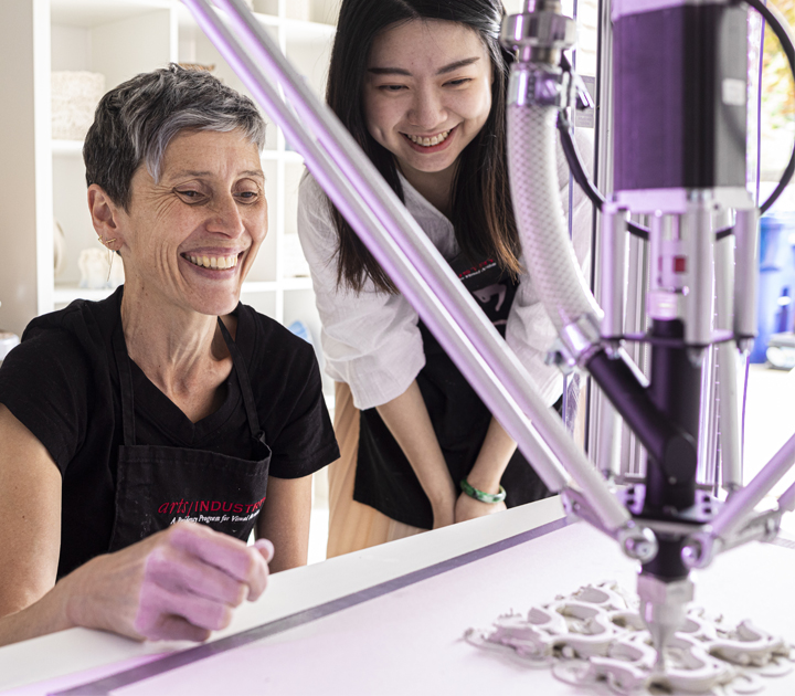 A smiling student and professor use a 3D printer that is using clay.