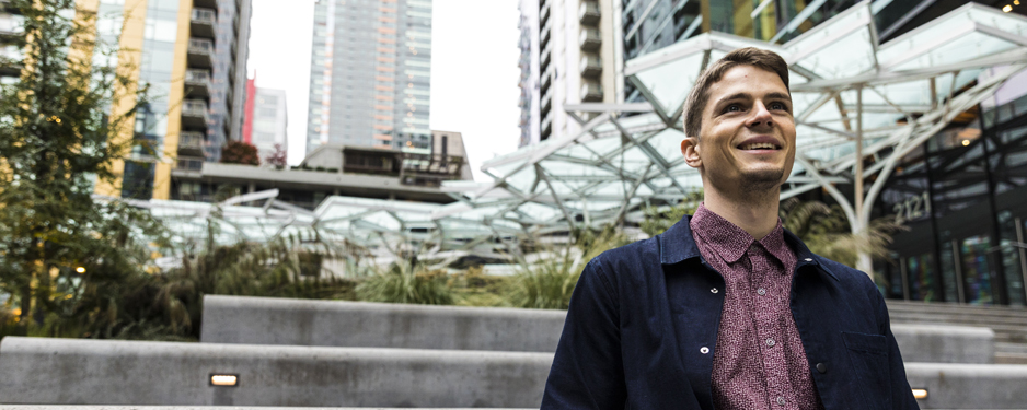 A smiling student stands in front of Amazon's buildings in downtown Seattle.