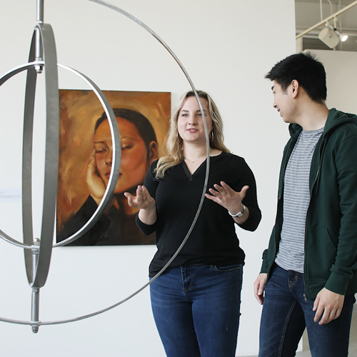 A male and female student look at a piece of art in the Jacob Lawrence Gallery.