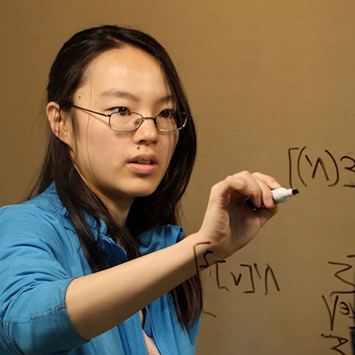 Student writing equations on a glass board.