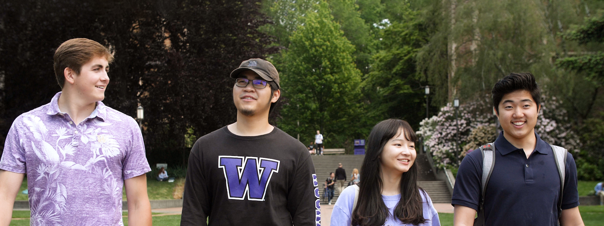 Four students side by side walk along Quad talking and laughing