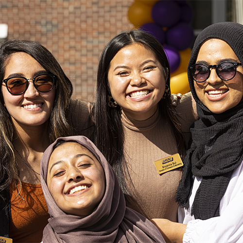 Group of four people smile widely with their arms around each other.