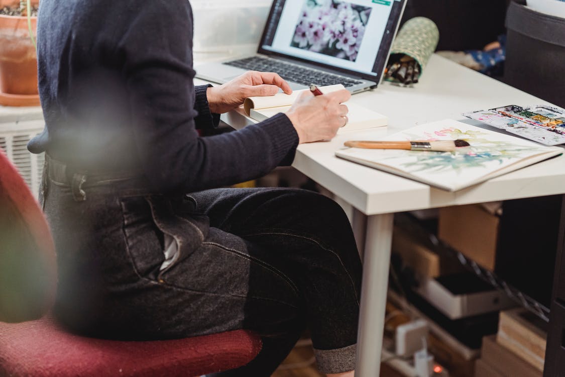 Person sitting at desk with laptop and sketchbook