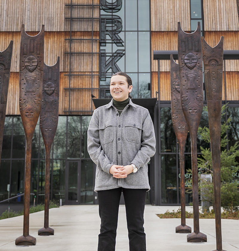 Male student standing in front of sculptures at entrance to the Burke Museum