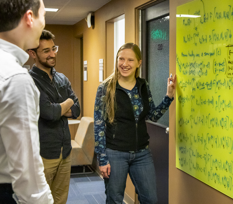 Three students smiling in front of yellow board with math equations