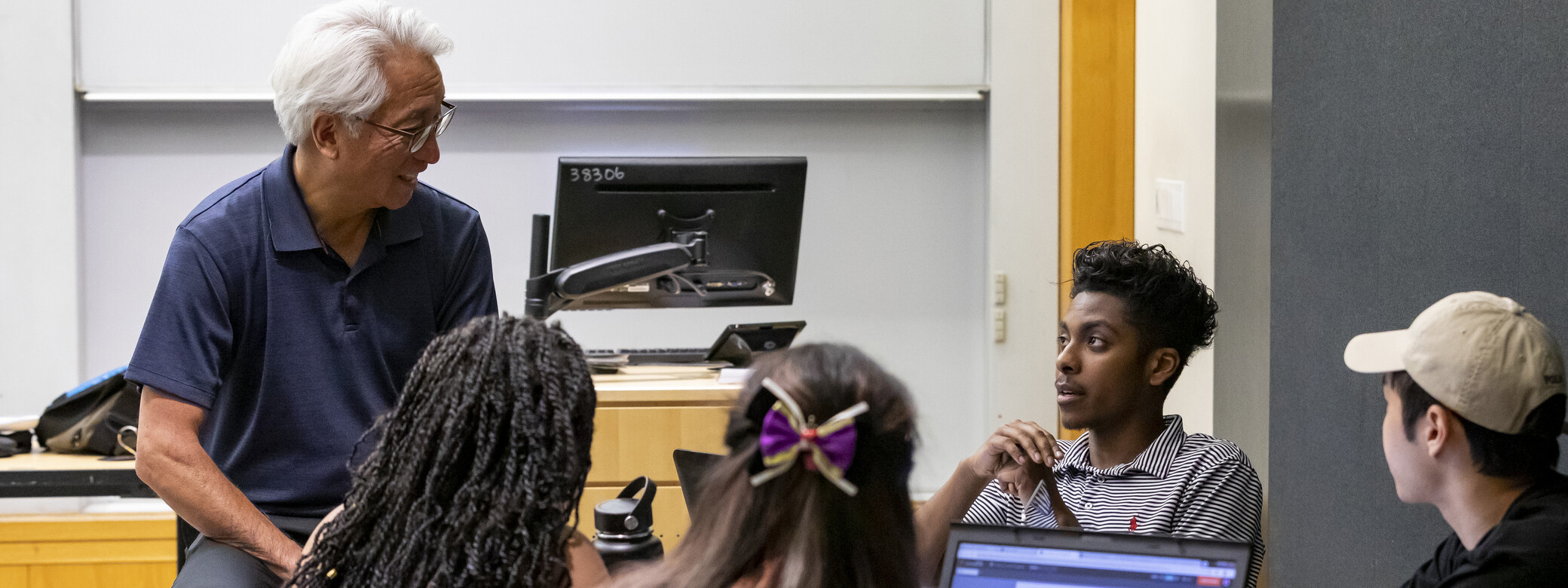 Male teacher talks to group of students in classroom