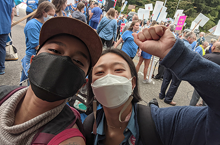 Sai Ahmed (left) and Soohyung Hur snap a self at a rally. Soohyung has a fist raised.