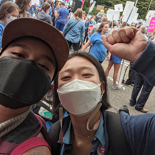 Sai Ahmed (left) and Soohyung Hur snap a self at a rally. Soohyung has a fist raised.