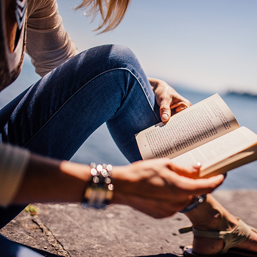 Woman reading outside, with a lake in the background.