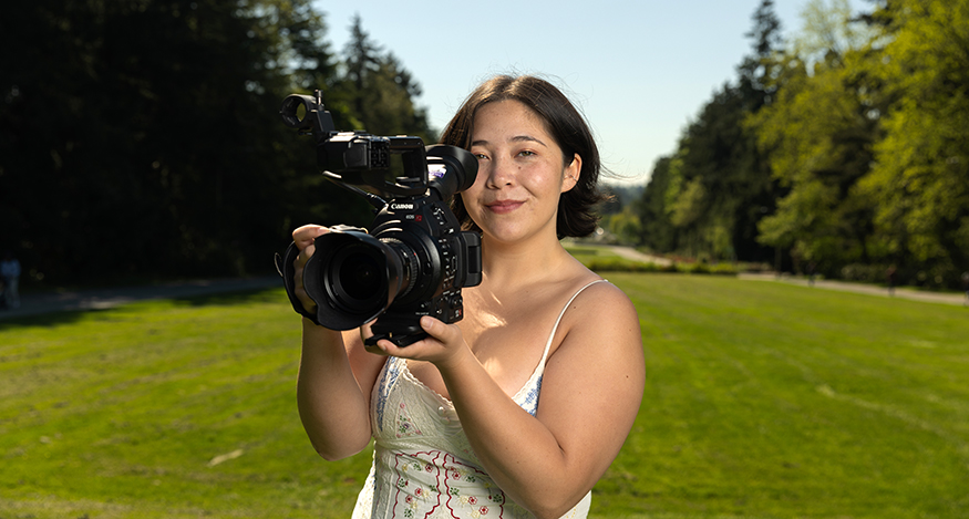 Kenna Fojas on the UW campus, holding a film camera to her face. 