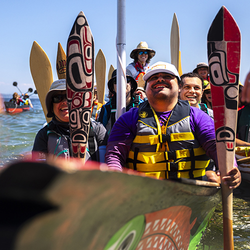 People holding traditional paddles in UW canoe.