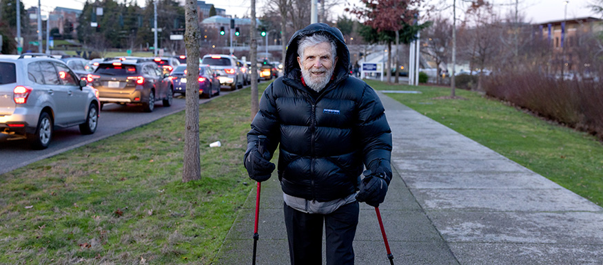 Marshall Baker in a down jacket walking to campus, using hiking poles for balance.