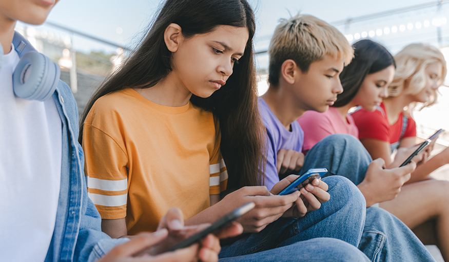 Teens sitting in a row, focused on their cellphones.