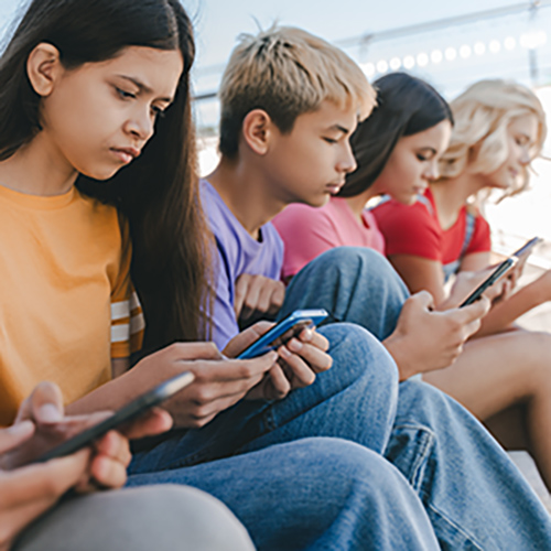 Teens sitting in a row, focused on their cellphones.