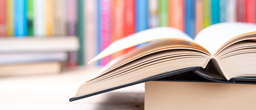 An open hardcover book with more books in the background.