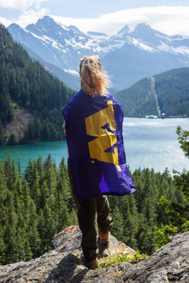 Tisbe Rinehart, viewed from behind, looks out at a mountain lake and snow-topped mountains beyond. 