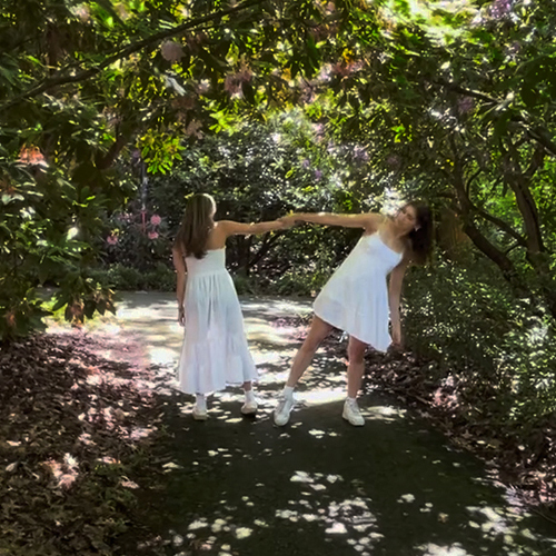 Two women in white, dancing in-between trees on the UW campus. 