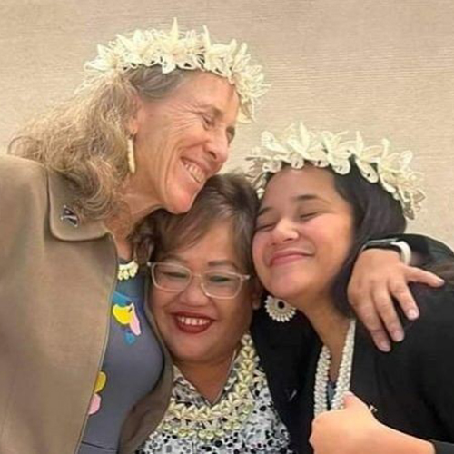 Holly Barker hugging two other women wearing flower garlands in their hair. 